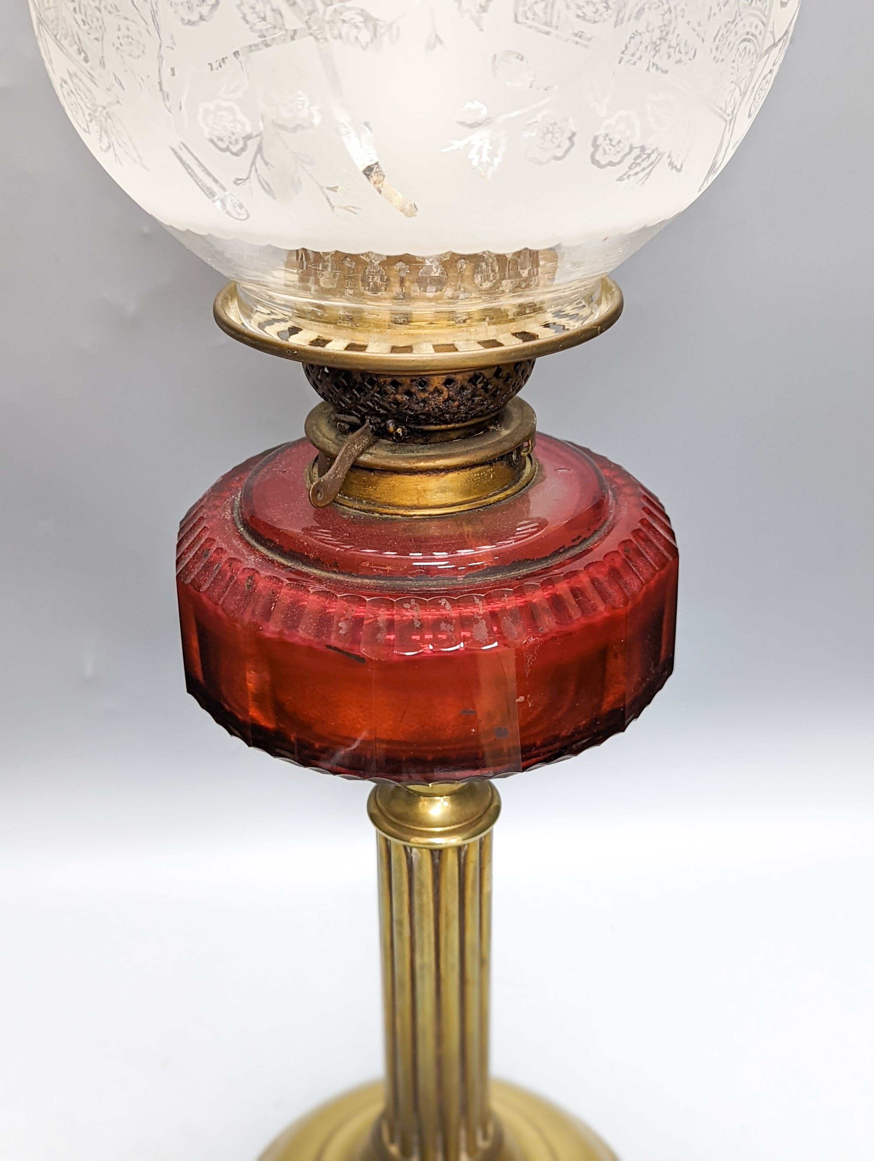 A Victorian brass oil lamp with etched glass shade and cranberry reservoir. 64cm total height
